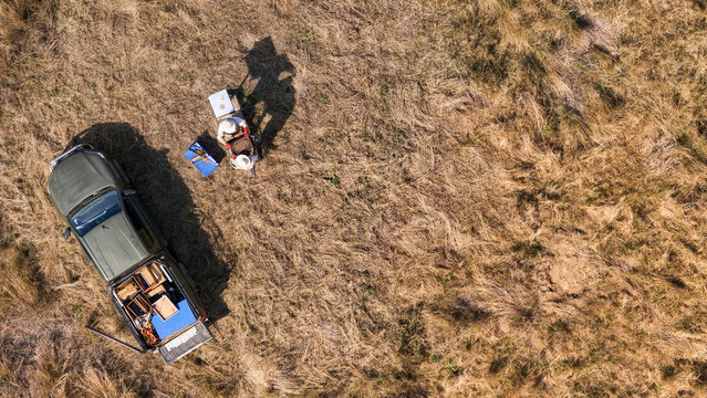Aerial view of a beekeeper working with beehives next to a pickup truck in a dry grassy field Pretoria, Gauteng, South Africa.