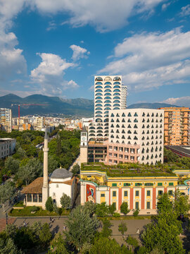 Aerial view of the Et'hem Bey Mosque and the Clock Tower with people walking on the sidewalk next to modern skyscrapers in Tirane, Tirana County, Albania.