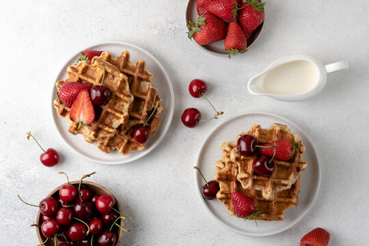 Fresh Belgian cottage cheese waffles served with strawberries and sweet cherries on a light table, top view. High protein breakfast or brunch concept featuring homemade waffles