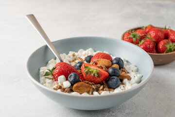 Fresh high protein cottage cheese berry bowl with blueberries, strawberries, chia seeds, granola and almonds served on light background with copy space © Anna Puzatykh