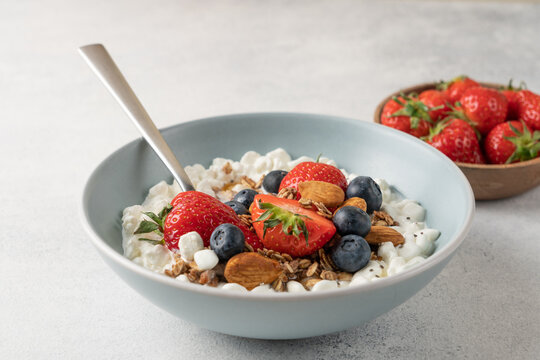 Fresh high protein cottage cheese berry bowl with blueberries, strawberries, chia seeds, granola and almonds served on light background with copy space