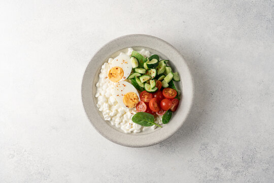 Fresh high protein savory cottage cheese bowl with cherry tomatoes, cucumber, boiled egg and chili flakes served on light background with copy space