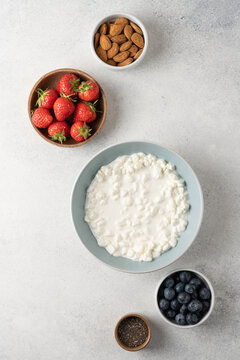 Fresh ingredients for a high protein cottage cheese bowl including blueberries, strawberries, chia seeds and almonds arranged on a light background with copy space