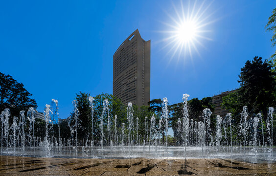 Courbevoie, France - 05 27 2026: Heatwave in Paris. Charras Park with a refreshing water feature and ground-level fountain, trees, buildings sun and blue sky in the background