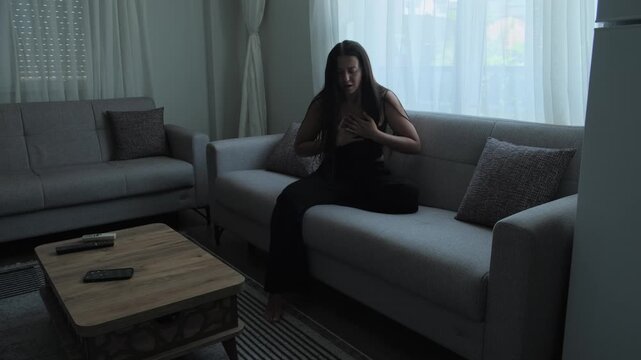 Woman experiencing panic attack and anxiety symptoms while sitting alone on sofa, emotional distress and mental health concept