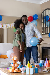 Obraz premium African American couple embracing in living room in front of coffee table with balloons, cupcakes