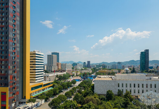 Aerial view of modern skyscrapers, the National History Museum, and lush green parks under a clear blue sky with mountains in the distance Tirane, Tirana County, Albania.