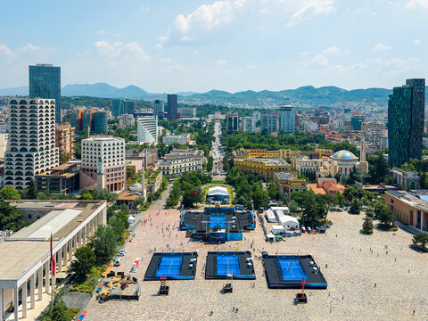 Aerial view of Skanderbeg Square featuring temporary tennis courts surrounded by historic buildings and modern skyscrapers under a clear sky in Tirane, Tirana County, Albania.