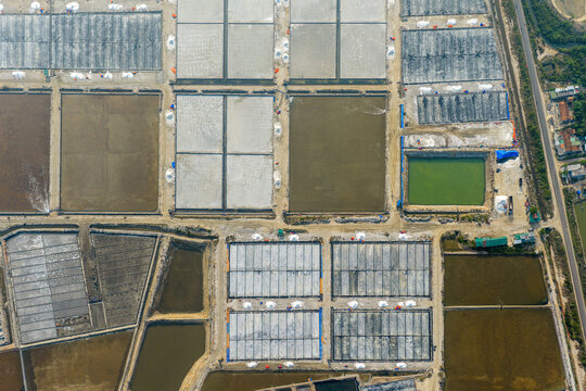 Aerial view of the geometric patterns of salt evaporation ponds with white salt crystals and dirt paths in Dong Hai, Ninh Thuan, Vietnam.