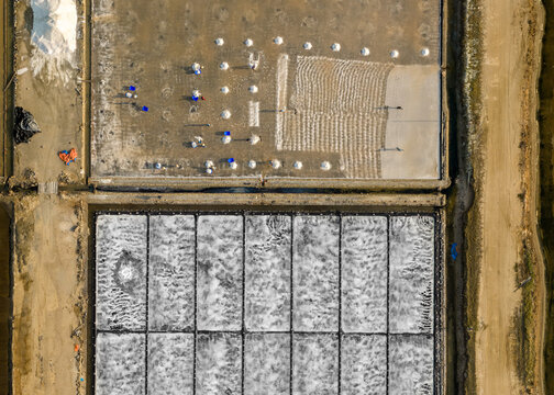Aerial view of salt pans with workers harvesting white salt mounds in a geometric grid pattern Dong Hai, Ninh Thuan, Vietnam.