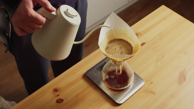 Man pouring water over full glass dripper coffee filter on kitchen scale