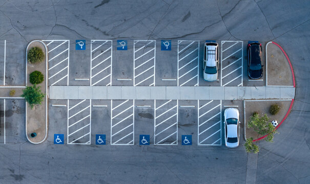 Aerial view of a parking lot featuring handicap spaces with blue symbols, parked cars, and small green bushes in Summerlin South, Nevada, United States.