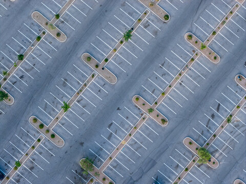 Aerial view of an empty parking lot with white painted lines and small landscaped islands with desert plants in Summerlin South, Nevada, United States.