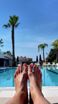 relaxing poolside view of feet on lounger with palm trees, summer vacation concept, vertical video