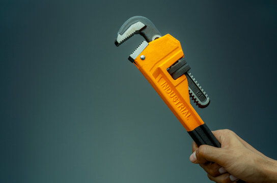 Plumber hand holding handle of chrome pipe wrench isolated on dark background. Metal monkey wrench for plumber. Mechanic tools. Hardware for fix and maintenance service. Clamping tools for plumbing.