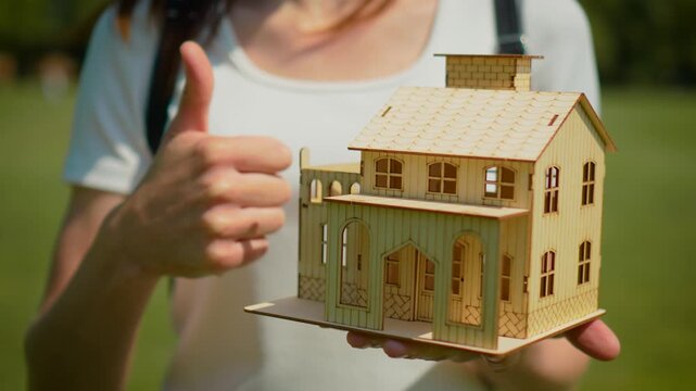 Housing approval concept with wooden house model and thumbs up gesture. Mortgage confirmation and successful property purchase idea with real estate investment planning. Home ownership satisfaction
