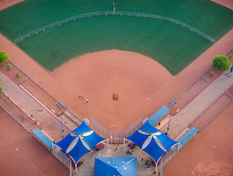 Aerial view of a baseball field with red dirt, green grass, and blue shade structures over the seating area Summerlin South, Nevada, United States.