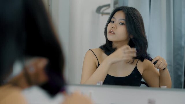 Young Asian female with straight black hair smiles as she combs her hair, she looking happy and refreshed. Cosmetics, beauty and hair care concept.