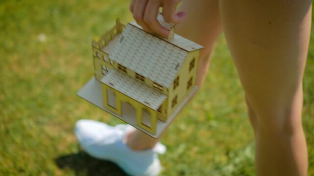 Housing relocation concept with miniature house carried in hands. Woman walking with wooden home model representing moving process and property transfer idea. Mortgage planning and new residence