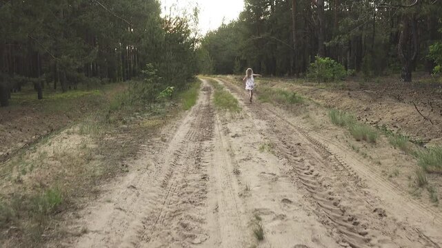 Two little sisters have fun run along country's lean of sandy road among pine boron.