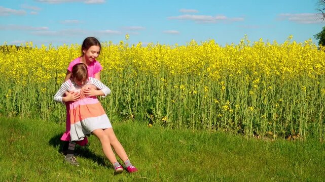 Two little sisters are playing against the backdrop of a large rapeseed field.