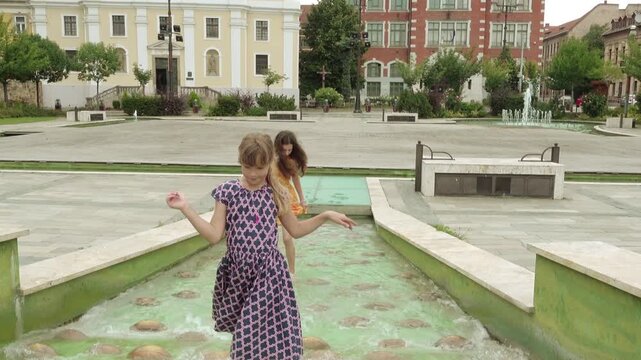 Two little beautiful girls walk in Fountain. Heroes Square in Miskolc, Hungary.