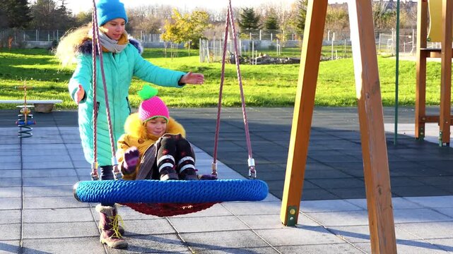 two beautiful girls ride a round swing in the autumn zoo