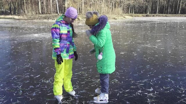 Slow motion. Two girls sisters skate on ice frozen lake. Winter city park.