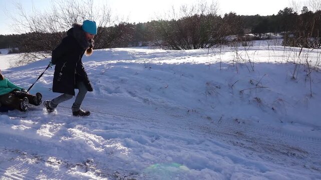 Slow motion beautiful girl in a winter jacket rolls her sister's on inflatable wheel in the snow.