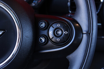 Obraz premium Close view of luxurious steering wheel buttons including central OK pad along with phone call voice activation and audio volume symbols on black leather. It emphasizes advanced vehicle cockpit technol