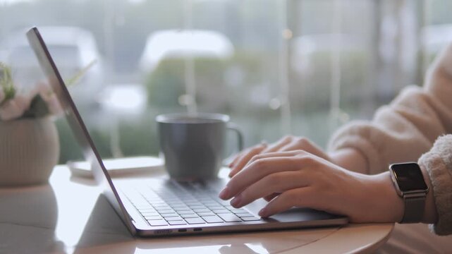 Person types on laptop, coffee mug beside. Natural light from window. Soft focus background. Peaceful, focused work vibe. Perfect for remote work, freelancing, or digital creativity themes