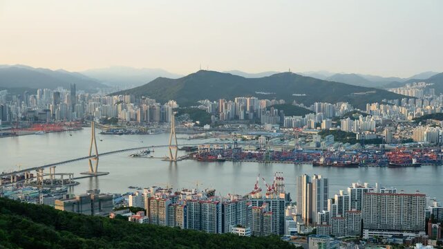 Day to Night Timelapse of Busan Harbor Bridge and busy Busan port with ship and car traffic , wide angle view from Bongrae Mountain. Busan is the second most populous city in South Korea.