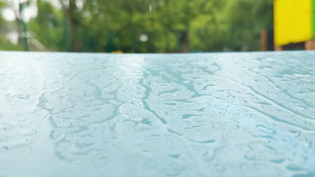 a wet blue swing seat moves slowly in the wind. The motion creates a soft metallic squeaking sound. Water droplets drip quietly from the edge.