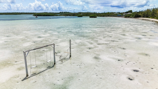 Aerial view of Turtle Beach featuring a wooden swing set and hammock in shallow turquoise water under a cloudy sky in Central Eleuthera, The Bahamas.