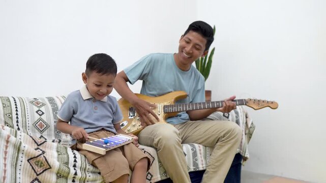 Happy father playing electric guitar while his little son plays xylophone at home, Father and son playing musical instruments together.