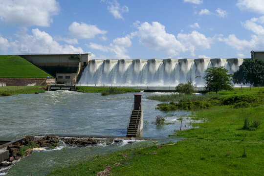 A wide dam spills water under a bright summer sky