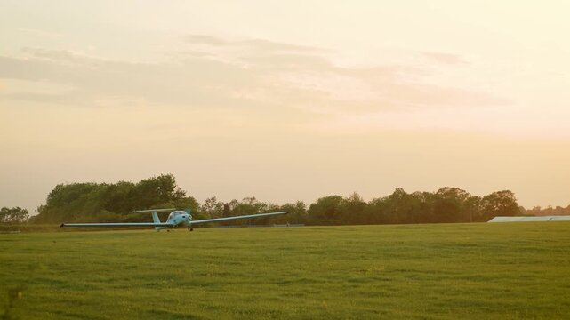 Light aircraft takeoff accelerating along grass runway at rural airfield during sunset. Frightened hare running across field beside small airplane preparing for departure. Aviation landscape featuring