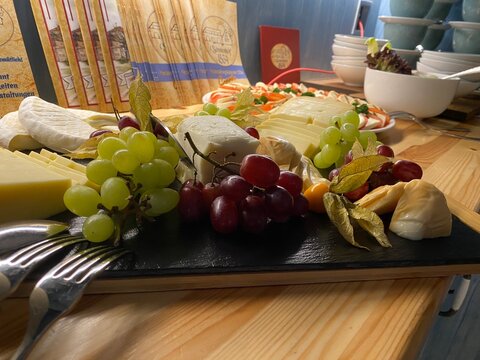 K&auml;seplatte mit Trauben, Feigen und verschiedenen K&auml;sesorten auf einem Holztisch. Genussvolle Feinkost, Buffet, Weinbegleitung und mediterrane Kulinarik. Authentisches Echtfoto.