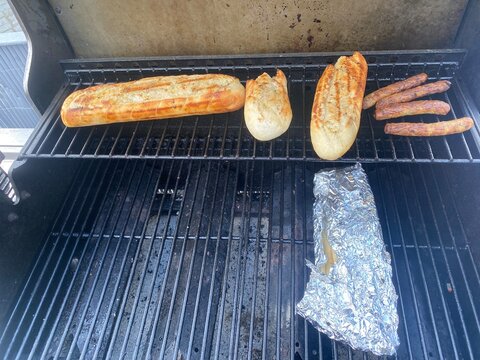 Grillgut auf einem Gasgrill mit Baguette, W&uuml;rstchen und Folienpaket. Authentisches BBQ-Motiv f&uuml;r Grillen, Sommer, Outdoor-K&uuml;che, Freizeit und geselligen Genuss. Echtfoto.