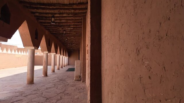 Ushaiqer Heritage Village showcasing traditional Najdi mud-brick colonnade and arches of the historic mosque. Walkway with authentic Arabian cultural architecture and shadows of Saudi Arabia
