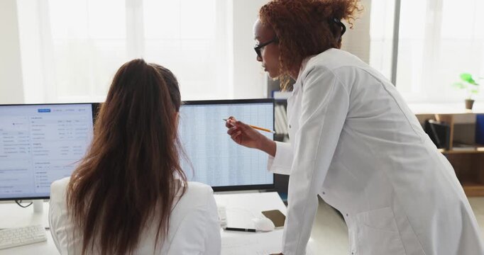 Doctors medical computer consultation analysis records teamwork healthcare. Senior physician guides colleague at workstation reviewing clinic data. Teamwork and accuracy in clinical care.