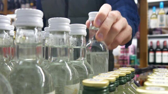 Close-up of many vodka bottles on an alcohol store display and a man with a shopping trolley choosing one
