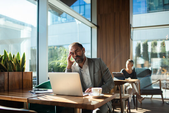 Businessman with headache working on laptop in cafe