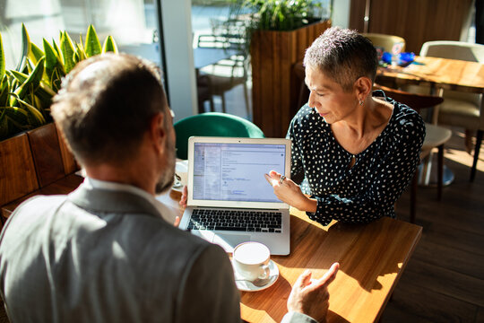 Two business professionals reviewing data on laptop together at cafe