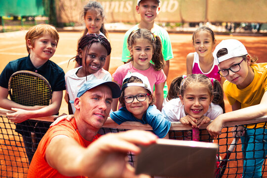 Tennis coach taking selfie with kids on clay court
