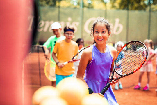 Smiling girl at kids tennis lesson on outdoor clay court