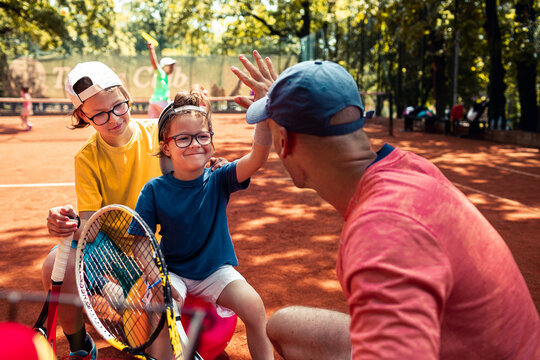 Tennis coach high-fiving children on outdoor clay court
