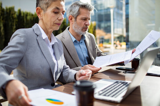 Senior business colleagues reviewing reports outdoors in a modern city