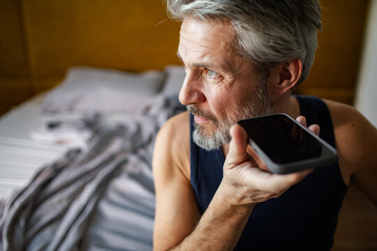 Mature man using smartphone voice command in bedroom