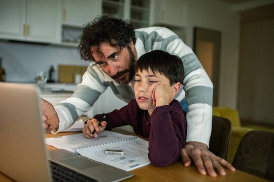 Father helping bored son with homework at kitchen table